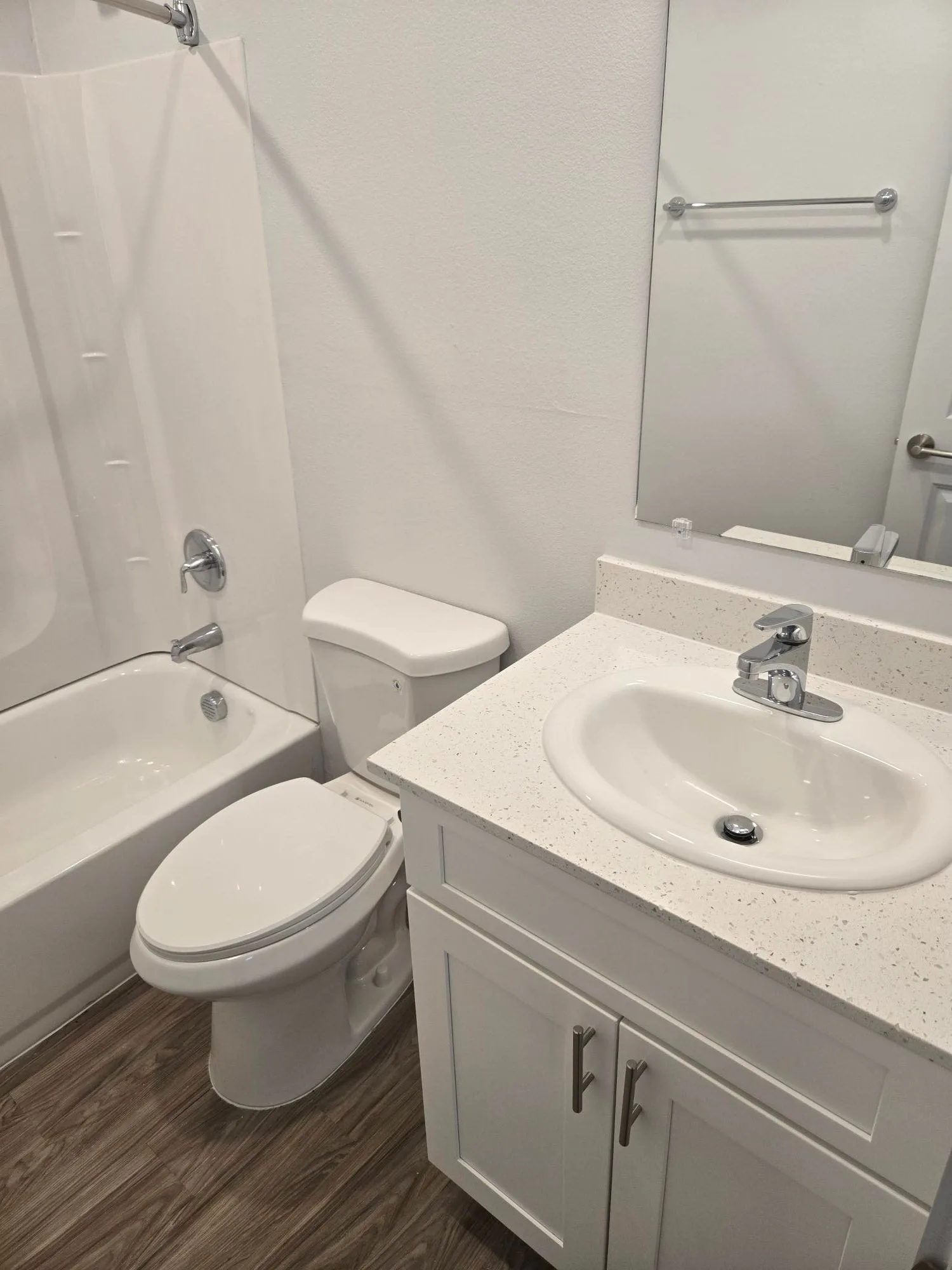 Renovated bathroom with a white countertop vanity, tub and shower combo and wood-look flooring
