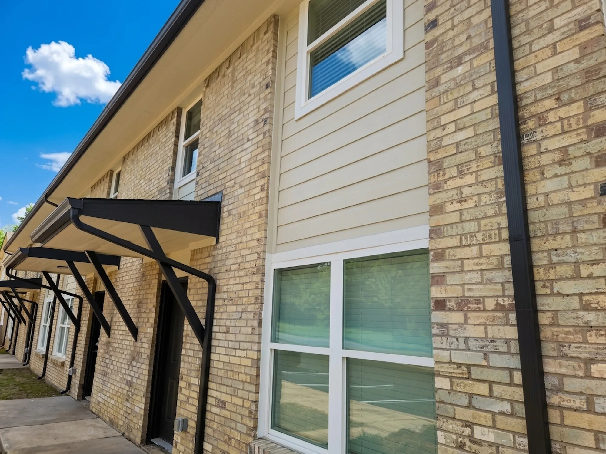 Blond brick and siding building with black steel awnings over the ground-floor entries