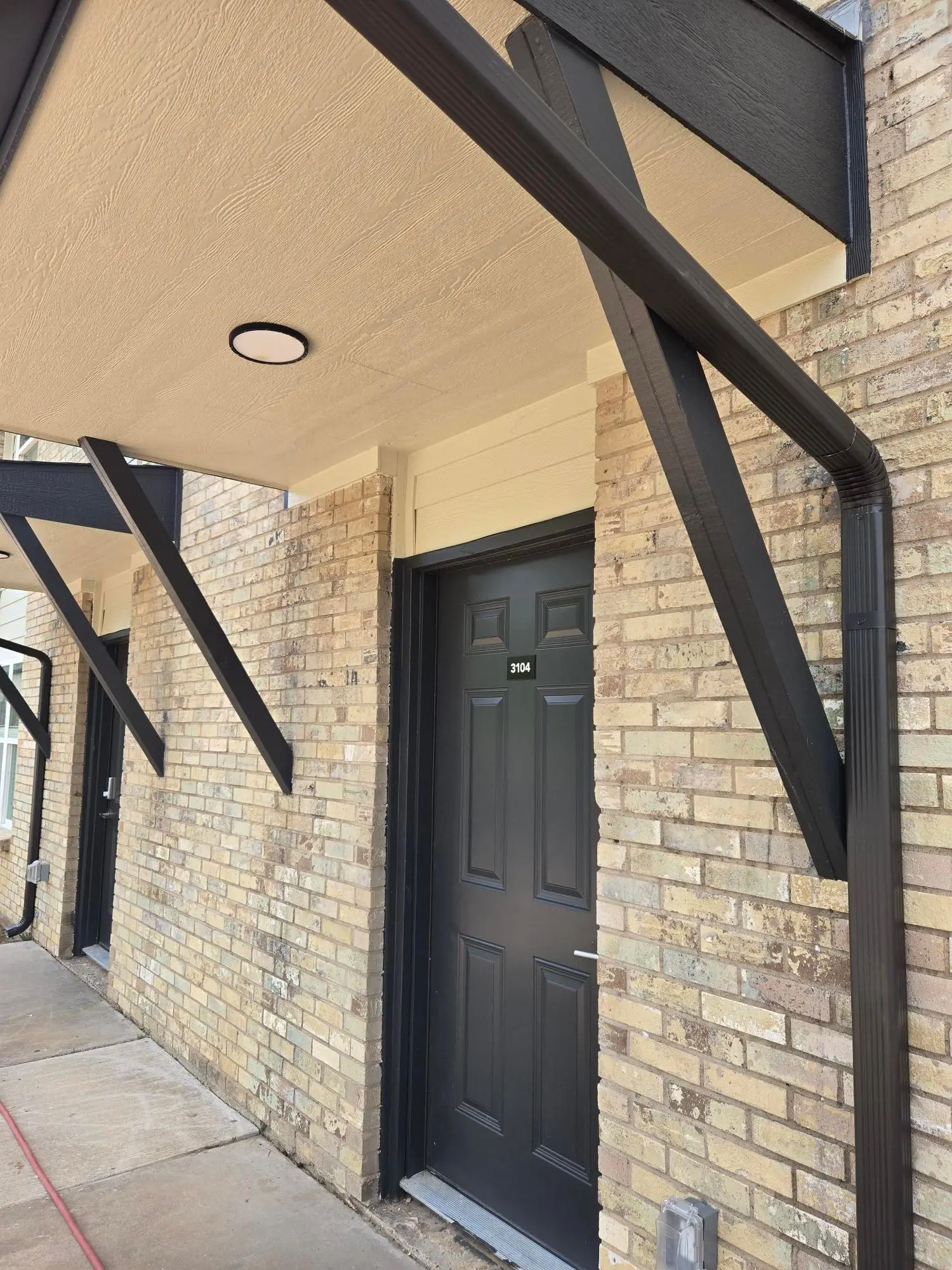 Charcoal apartment entry door beneath a new black steel awning set into blond brick masonry