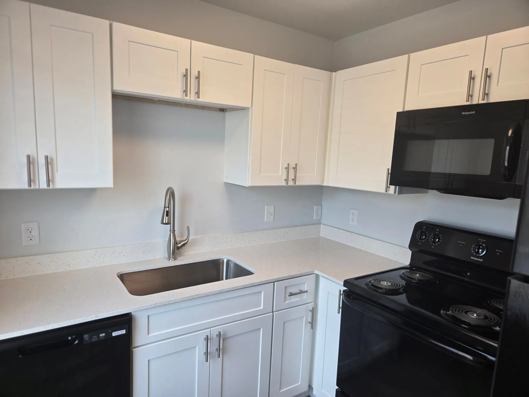 Renovated kitchen with white shaker cabinets, white counters and black appliance package
