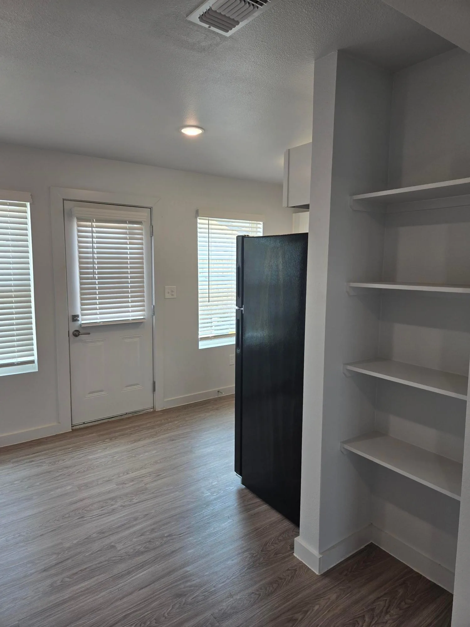 Built-in pantry shelving beside the refrigerator in a renovated kitchen corner with plank floors