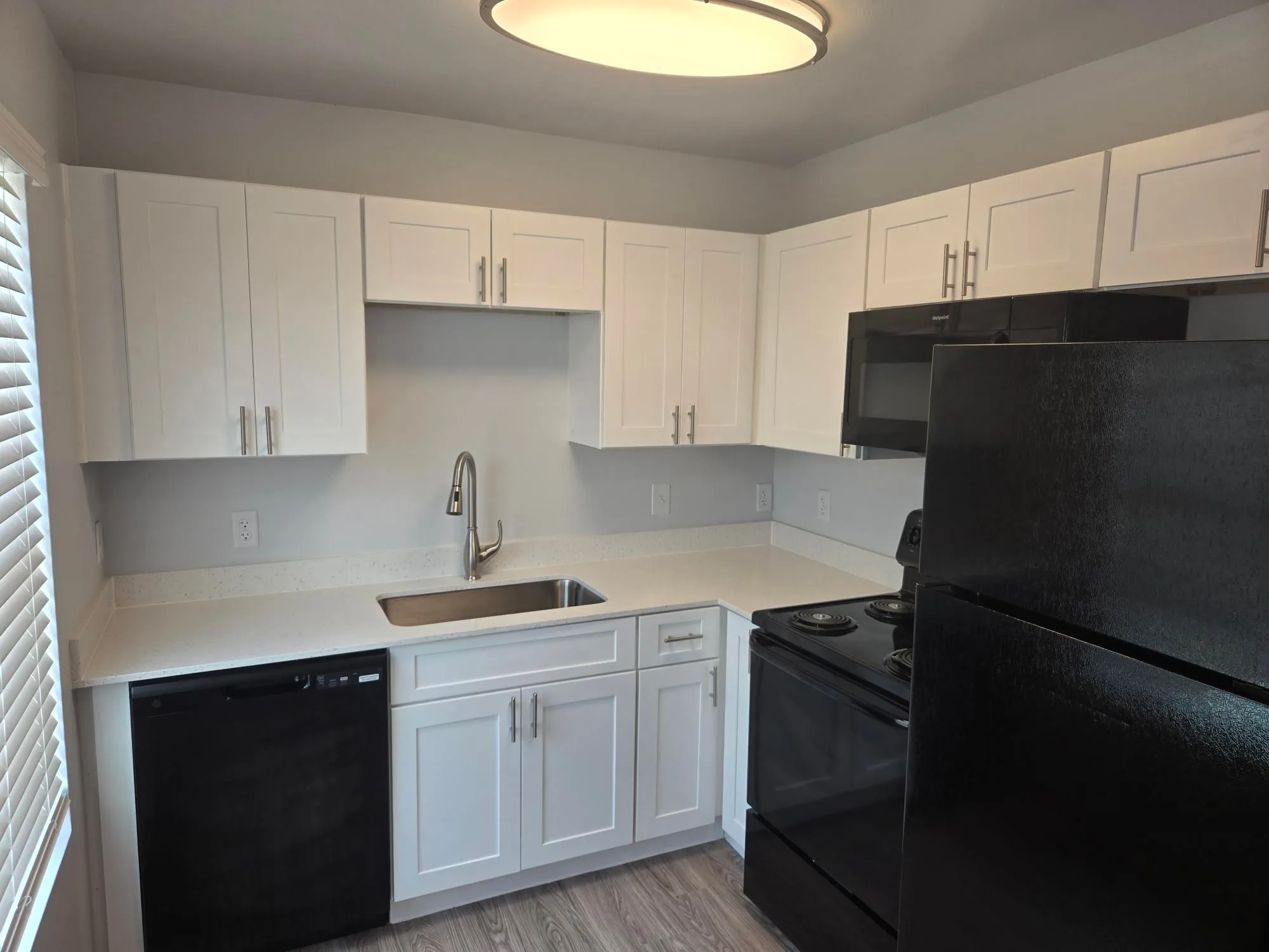Galley kitchen with white shaker cabinets, black appliances and speckled white countertops