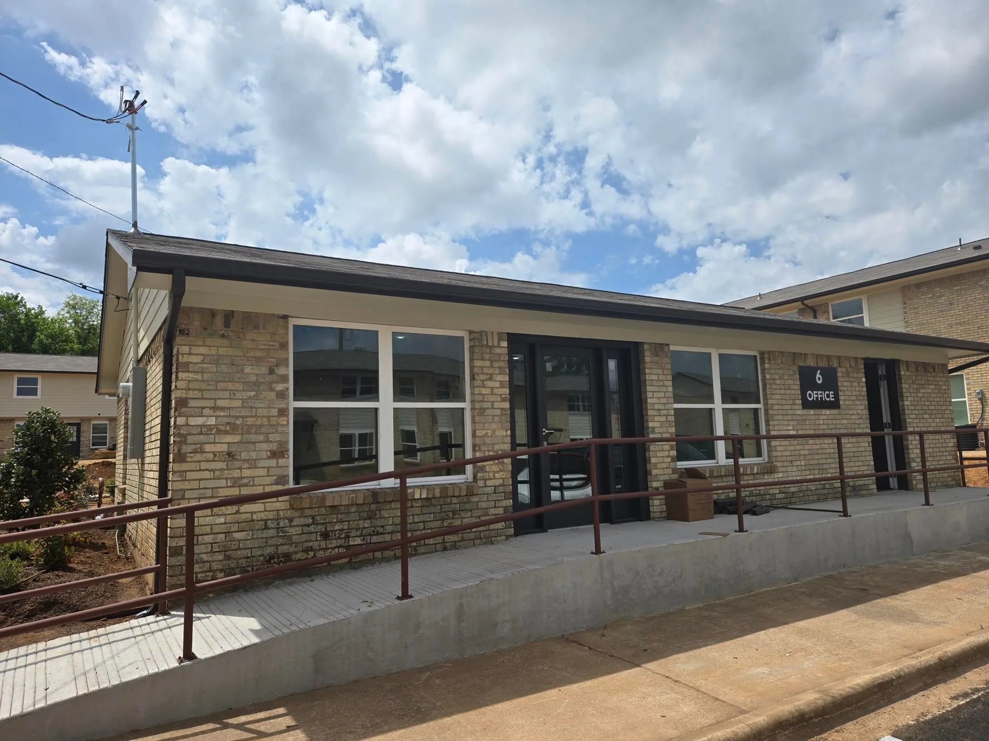 Single-story leasing office in tan brick with large windows and an ADA-accessible entry ramp