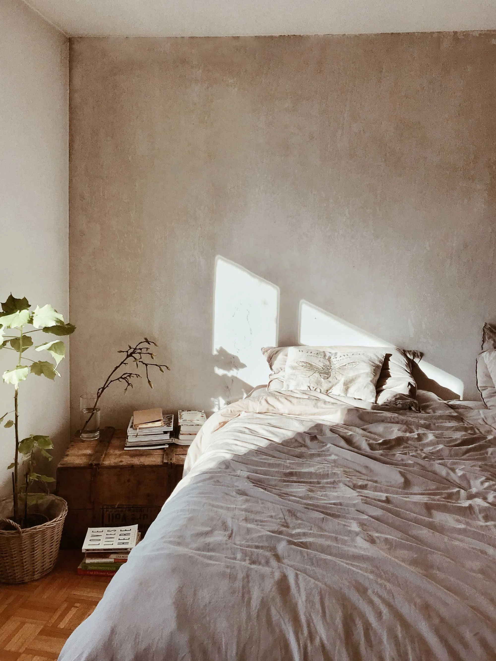 Soft morning light falling across a bed dressed in rumpled natural linen beside a wood nightstand