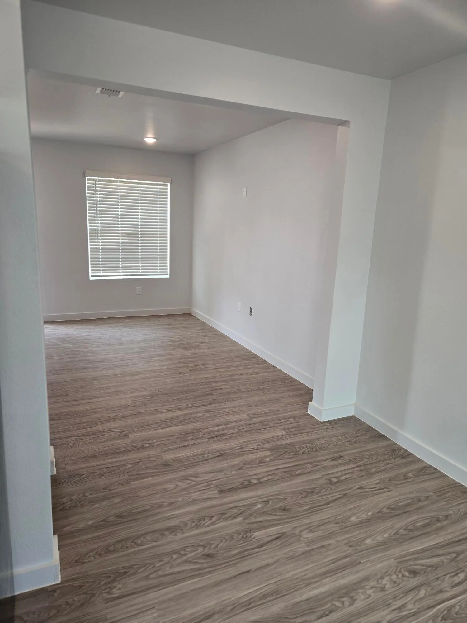 Spacious living and dining room with wood-look plank flooring and a bright window with blinds