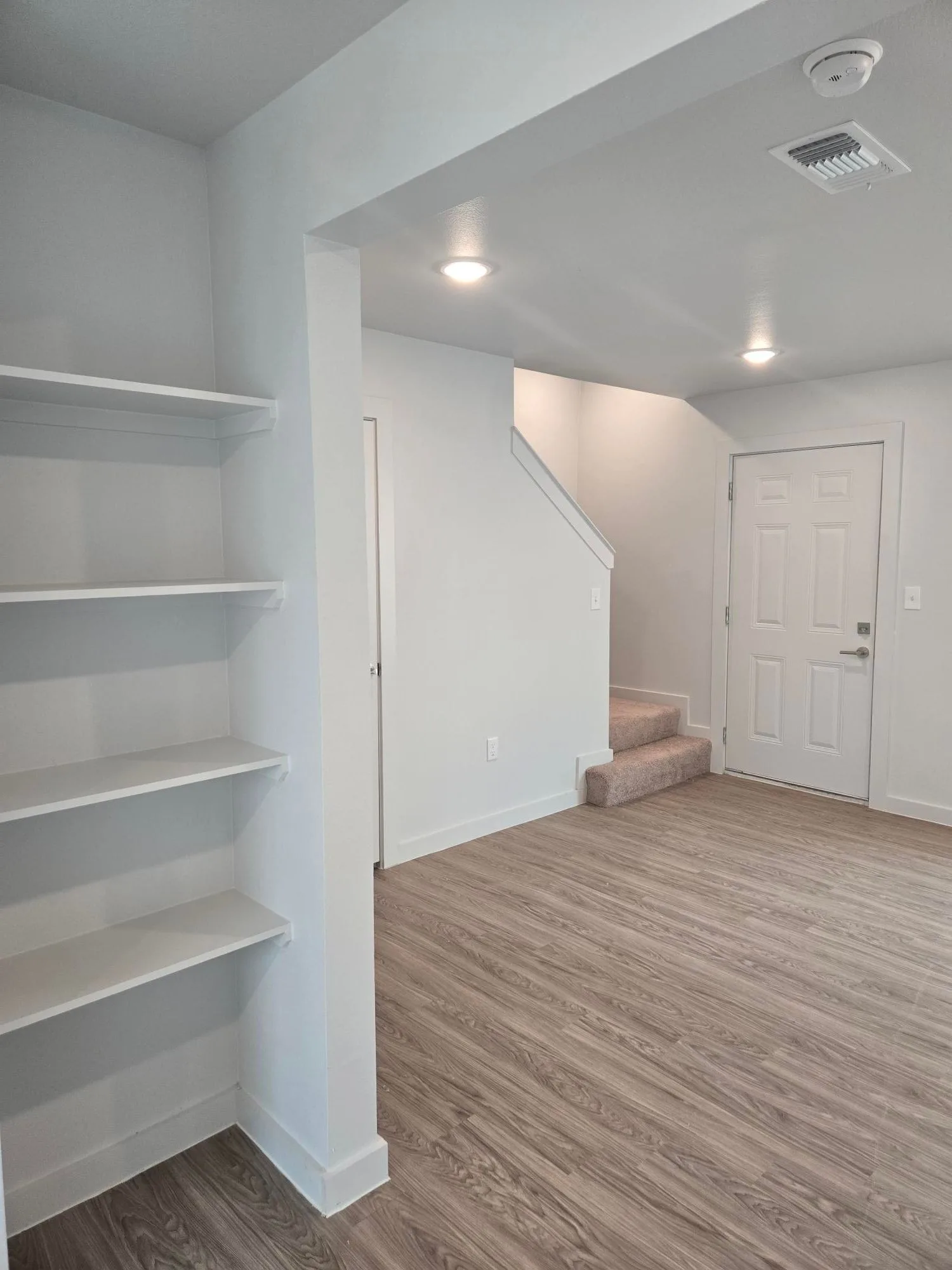 Entry living space with built-in shelving, wood-look plank floors and a carpeted staircase