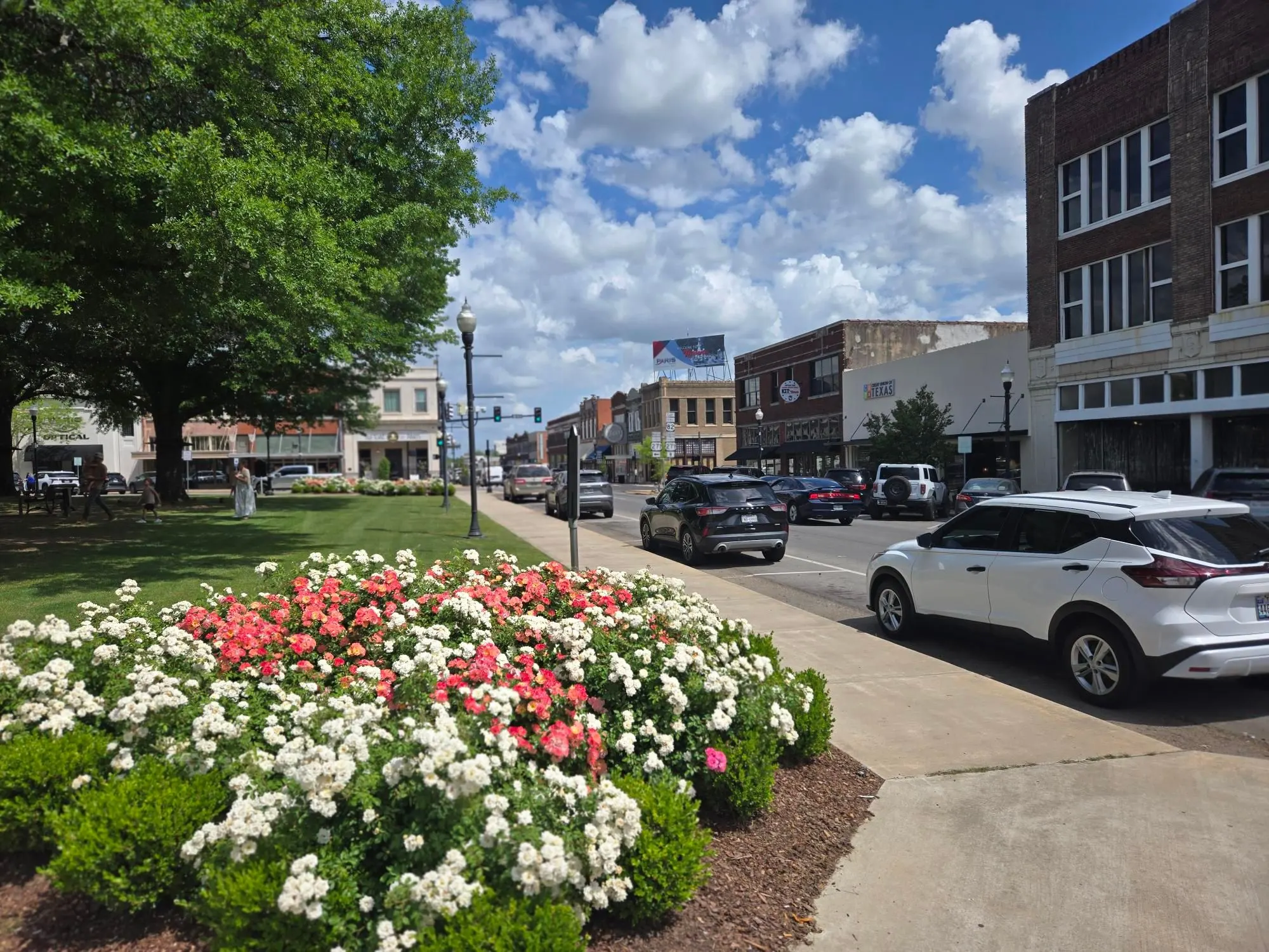 Parked cars and brick storefronts lining the rose-planted median at the downtown Paris square