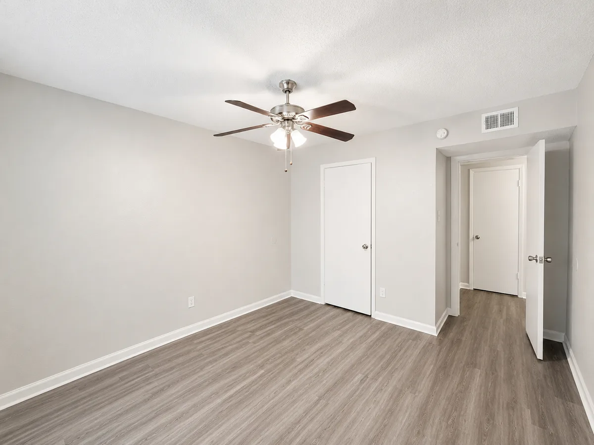 Bedroom with ceiling fan and closet, opening to a hallway with wood-look flooring