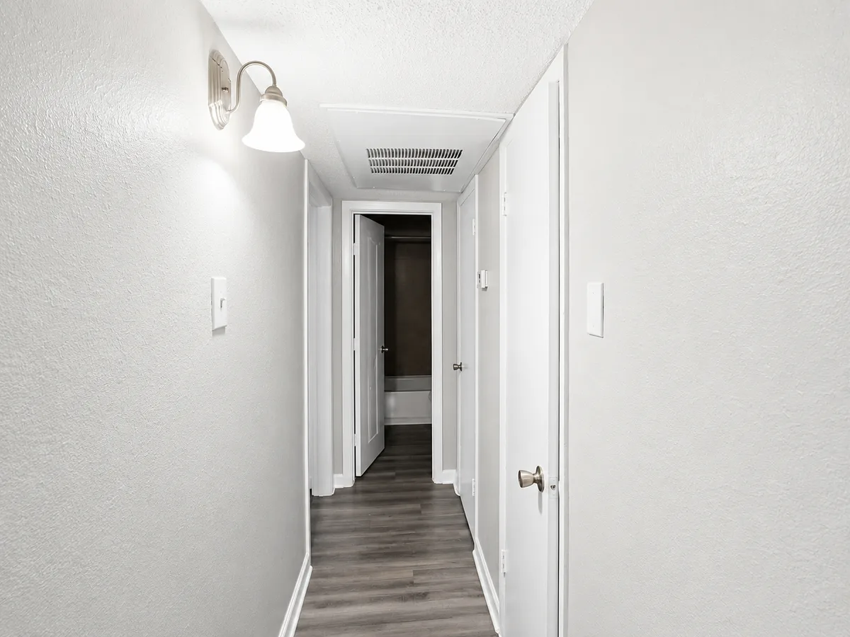 Interior apartment hallway with wood-look flooring, sconce lighting, and doors to the bathroom