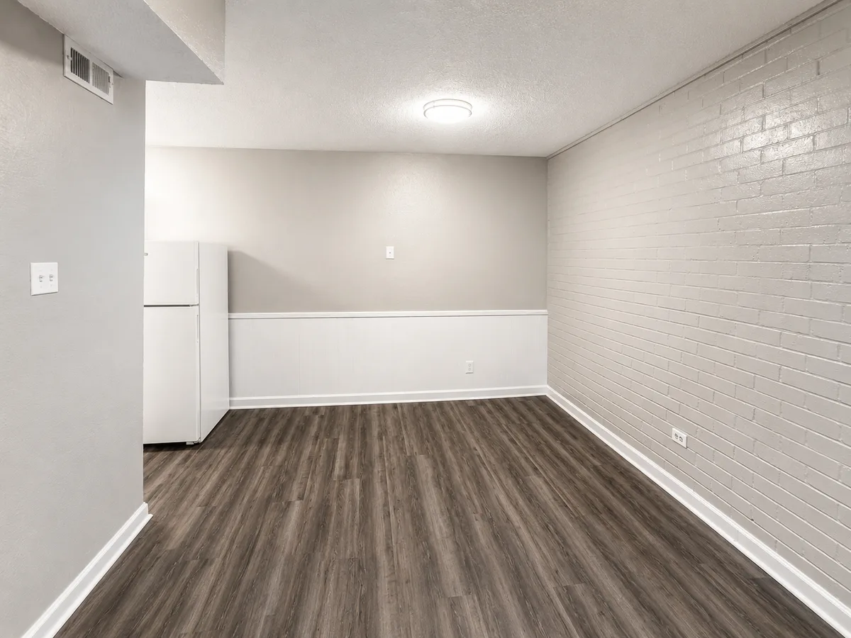 Open living and dining space with painted brick wall, wainscoting, and wood-look flooring