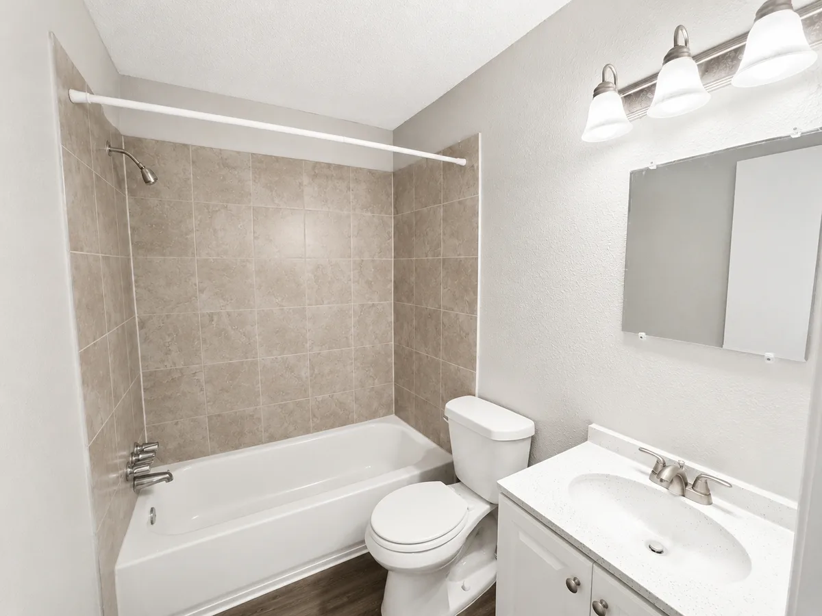 Bathroom with stone-look tiled tub-shower, white vanity, and wall-mounted mirror