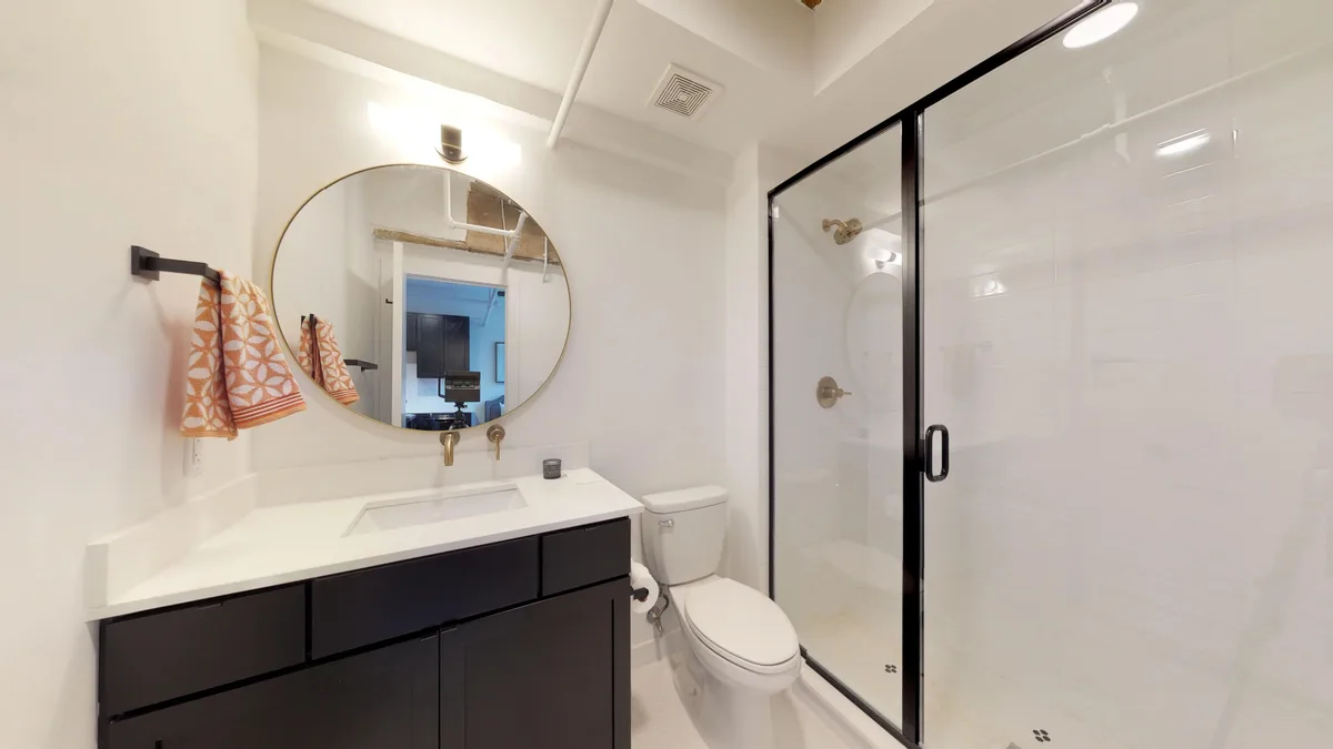 Bathroom with round mirror, black vanity, quartz counter and a glass-enclosed walk-in shower