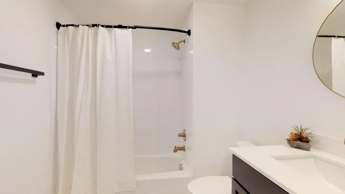 Bathroom with white subway-tiled tub and shower, black fixtures and a quartz-topped vanity
