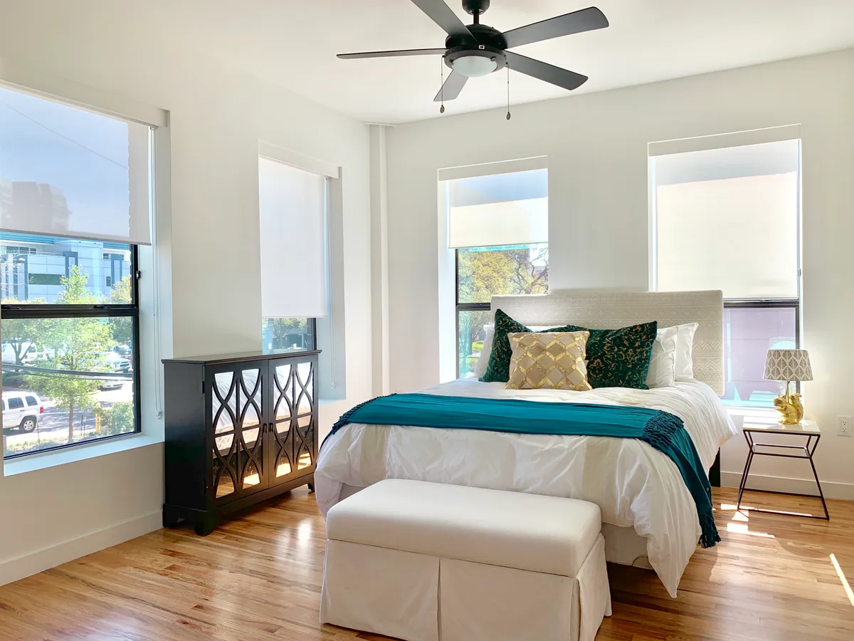 Bright bedroom with ceiling fan, three windows, hardwood floors and a mirrored accent chest