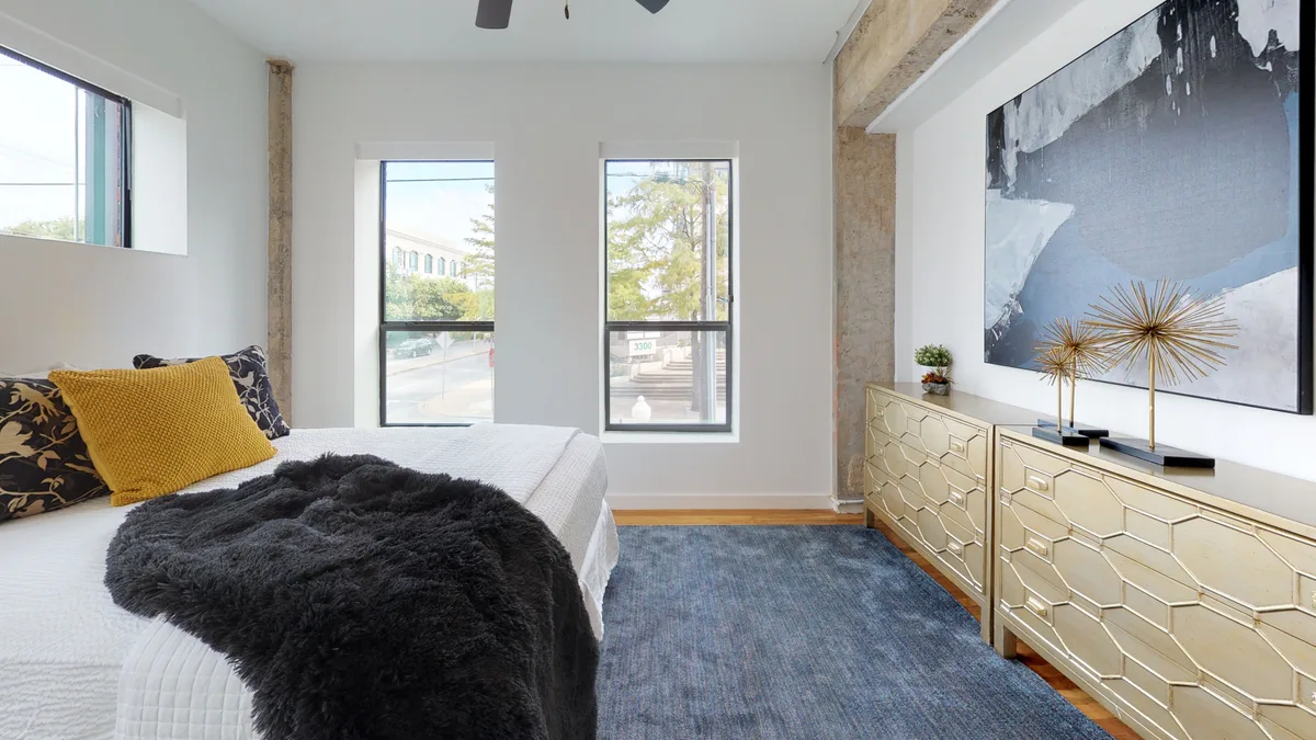 Bedroom with gold dressers, framed abstract art, an exposed column and tall street-facing windows