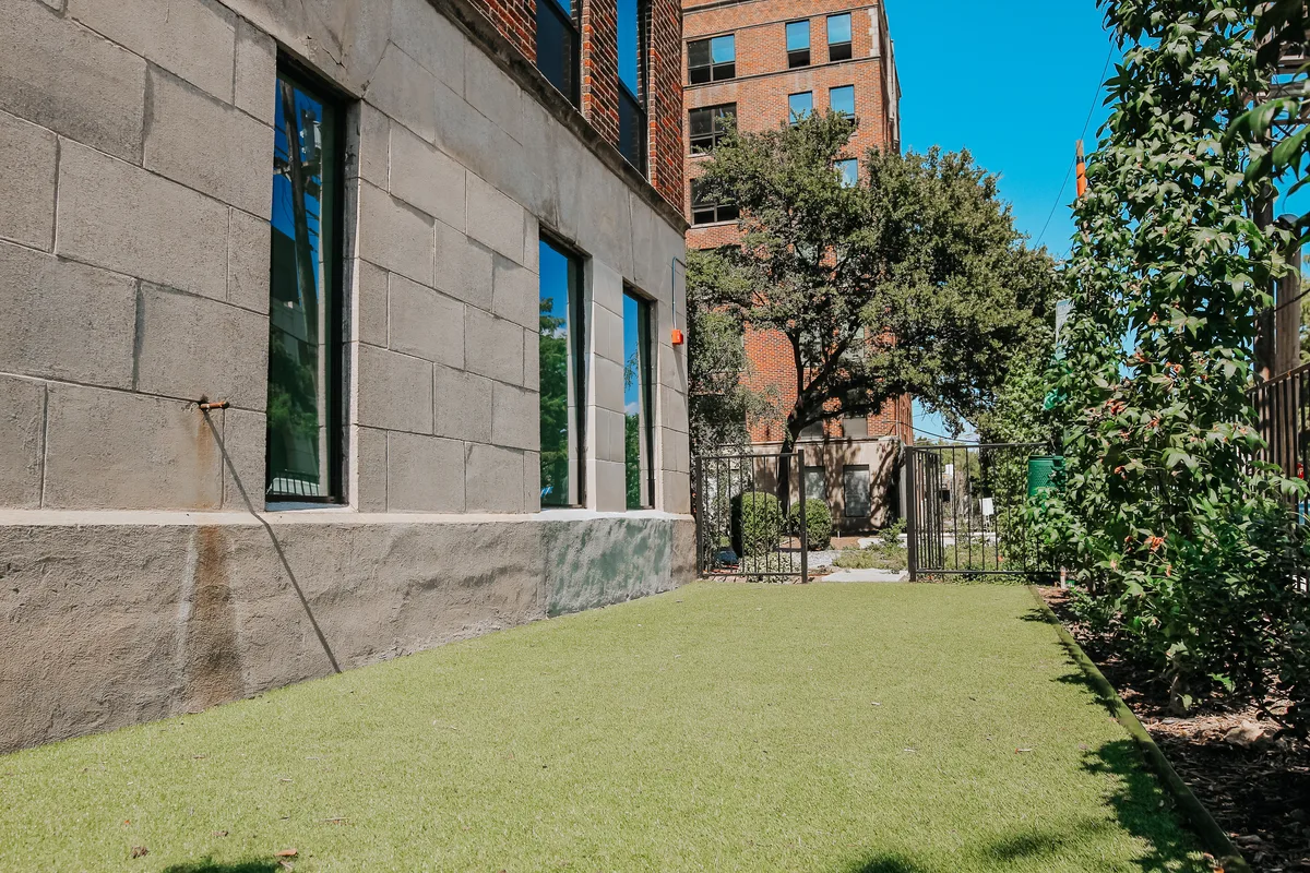 Fenced artificial-turf dog run alongside the building with mature trees and a gated entry