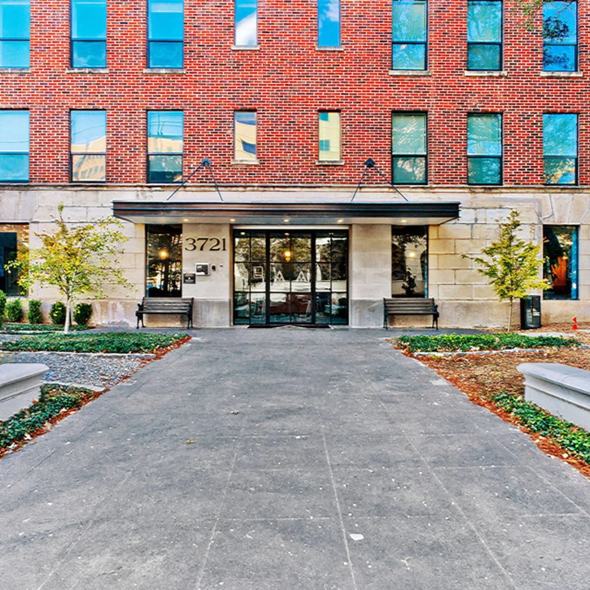 Front entrance with steel canopy, engraved address, flanking benches and landscaped walkway along the brick facade
