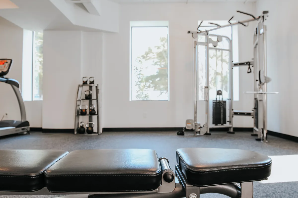 Fitness center with treadmill, cable weight machine, kettlebells and free weights beneath bright windows
