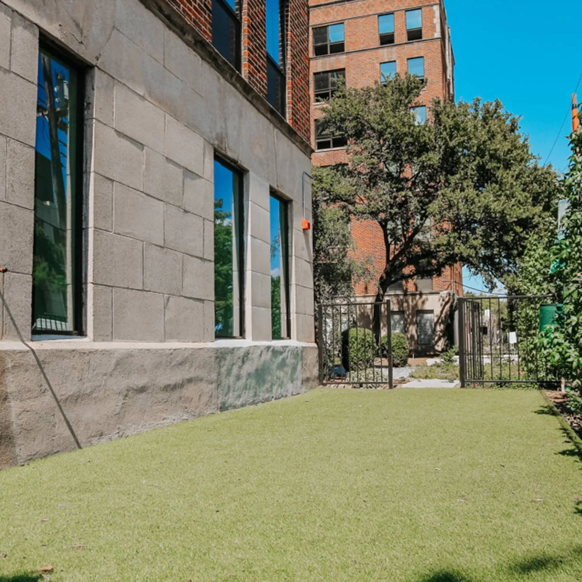 Landscaped turf lawn beside the building's stone base with a gated garden and shade tree