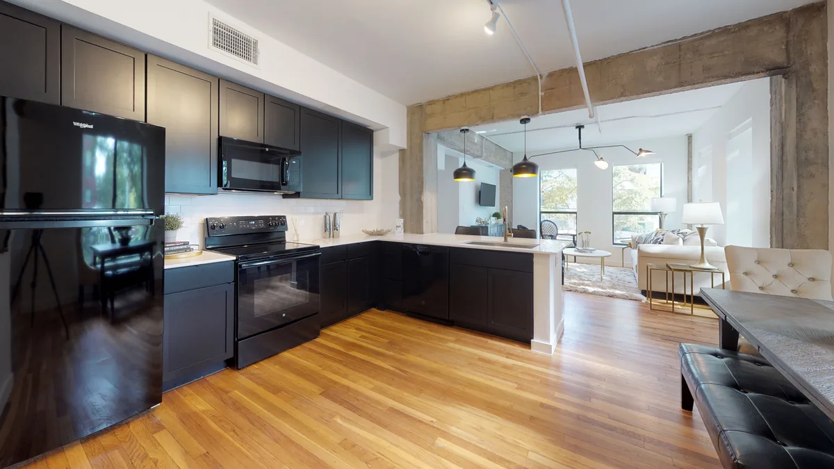 Loft kitchen with black appliances, subway-tile backsplash and quartz peninsula open to the living space