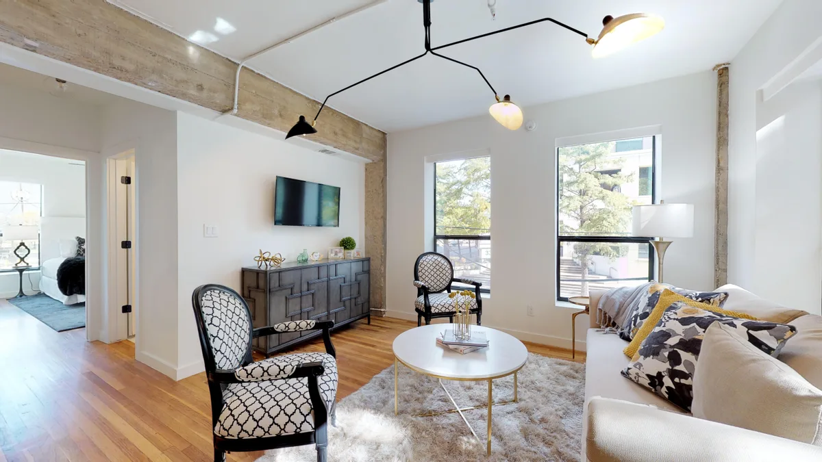 Staged living area with exposed concrete beam, hardwood floors, wall-mounted TV and large windows