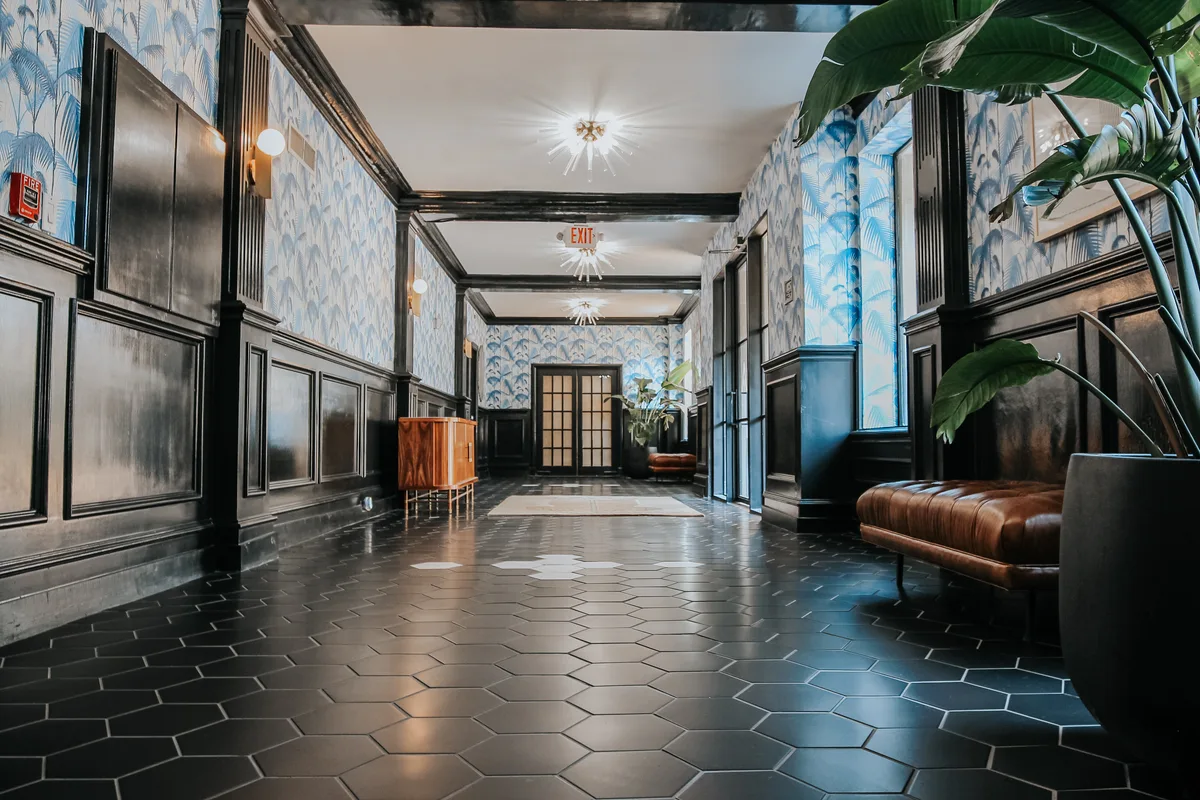 Main lobby corridor with black hexagonal tile, palm-print wallpaper, leather benches and French doors