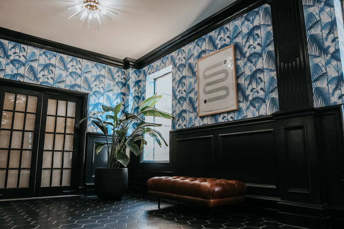 Entry vestibule with blue palm-print wallpaper, black wainscoting, leather bench and a sunburst light fixture