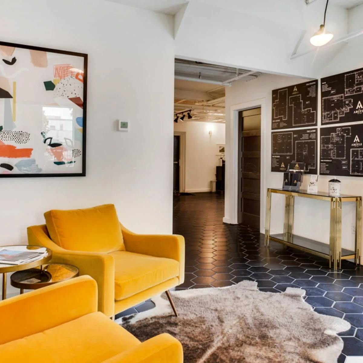 Leasing lounge with mustard velvet chairs, abstract art and floor-plan display over black hex tile