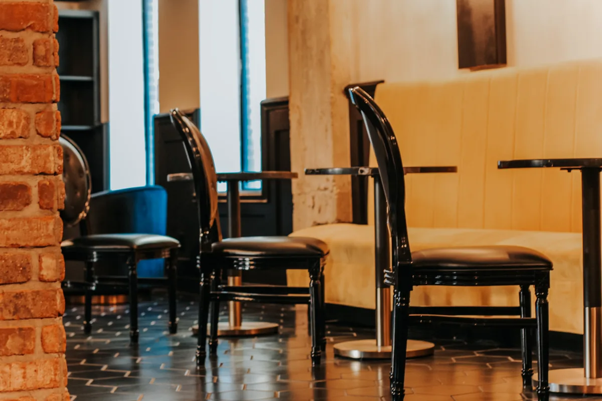 Speakeasy lounge with black bentwood chairs, gold velvet banquette and an exposed brick column