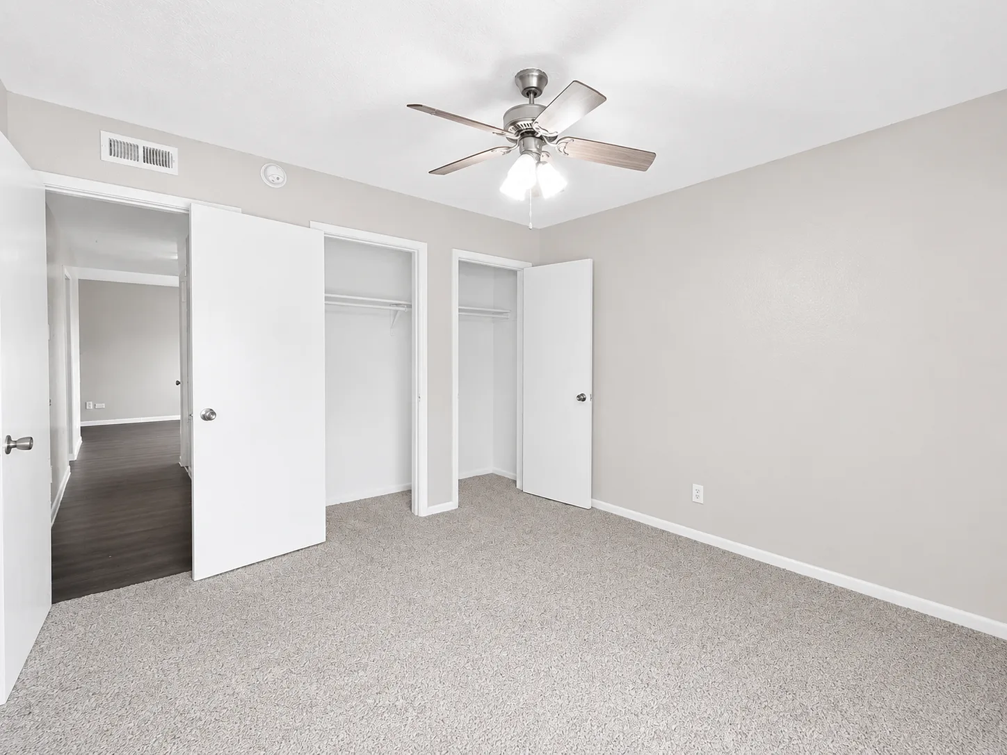 Empty carpeted A1 bedroom with a ceiling fan and two closets, one with sliding doors and one with a hinged door