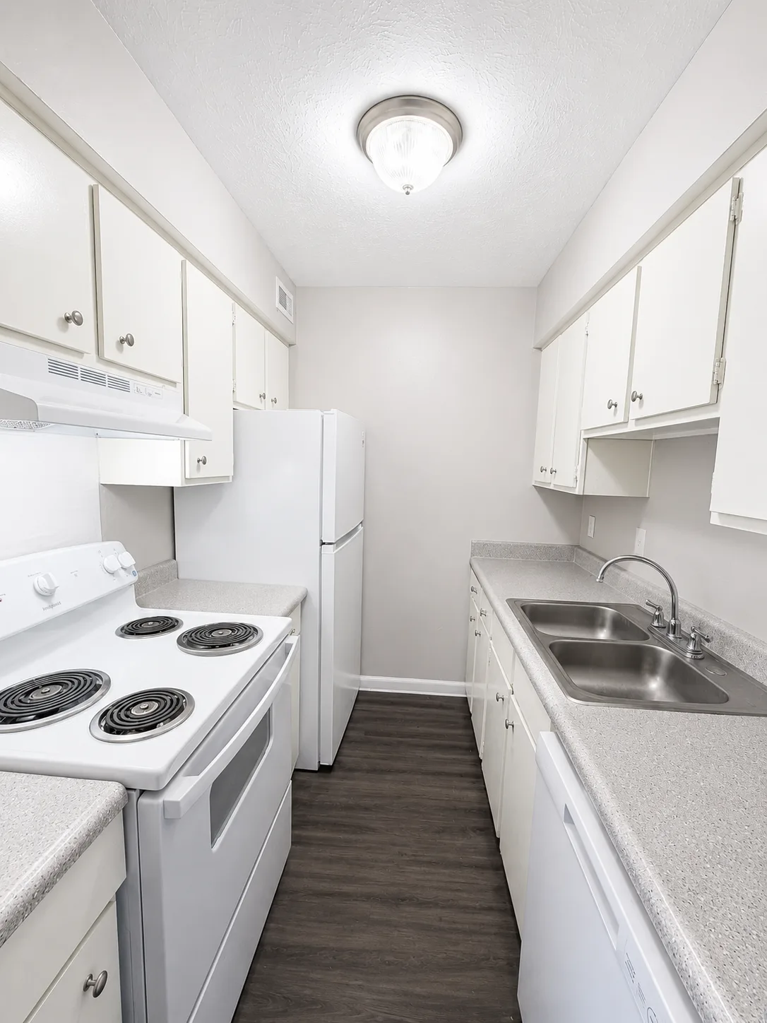 A1 galley kitchen with white cabinets, a white electric range, refrigerator and dishwasher, speckled counters and a double stainless-steel sink