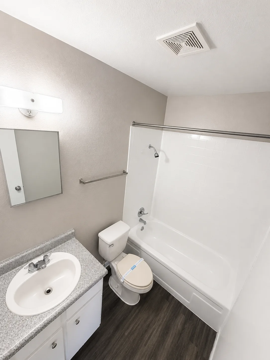 B1 full bathroom with a white-tiled tub and shower, a speckled-top vanity with a framed mirror, and wood-look flooring