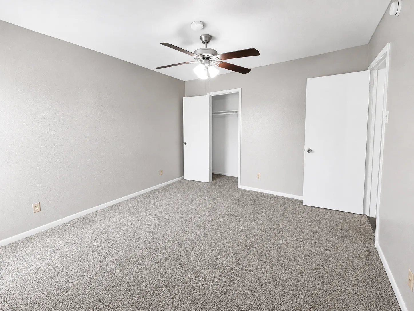 Empty carpeted B1 bedroom with a ceiling fan and an open closet with a hanging rod