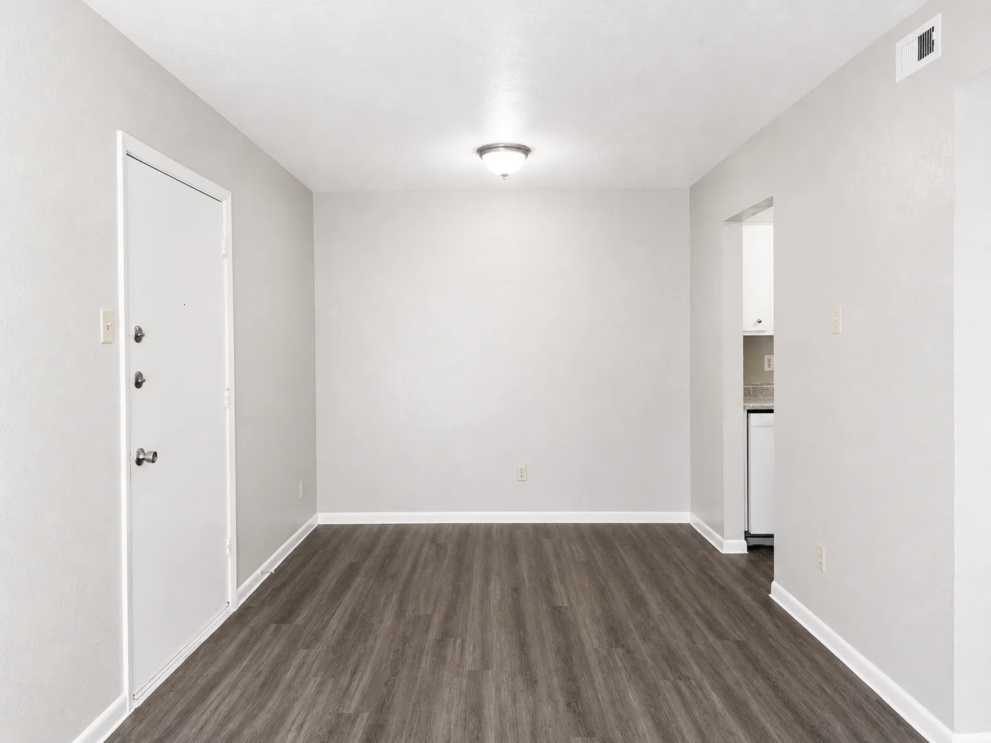 Empty B1 entry and dining area with the front door on the left and a pass-through to the kitchen on the right