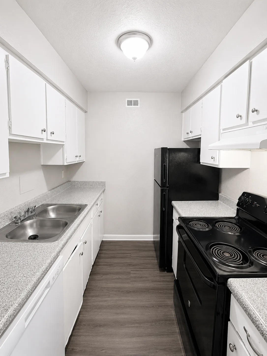 B1 galley kitchen with white cabinets, a black refrigerator and electric range, speckled counters and a double stainless-steel sink