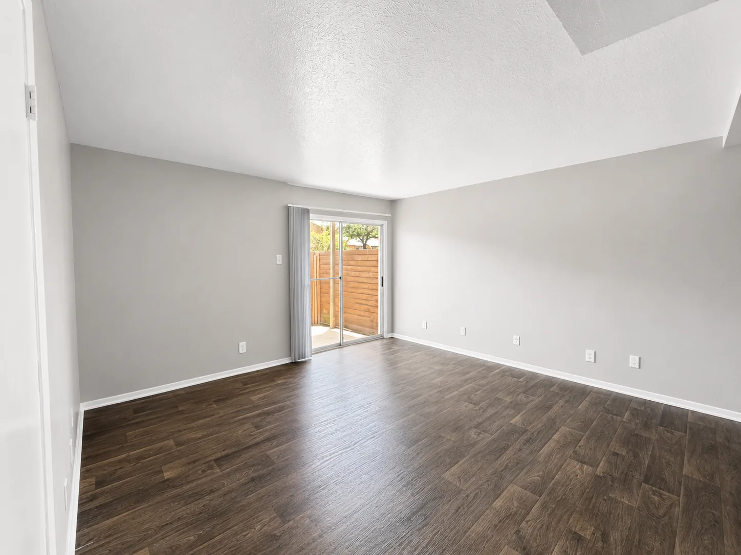 Empty B1 living room with a sliding glass door opening to a wood-fenced private patio and wood-look flooring