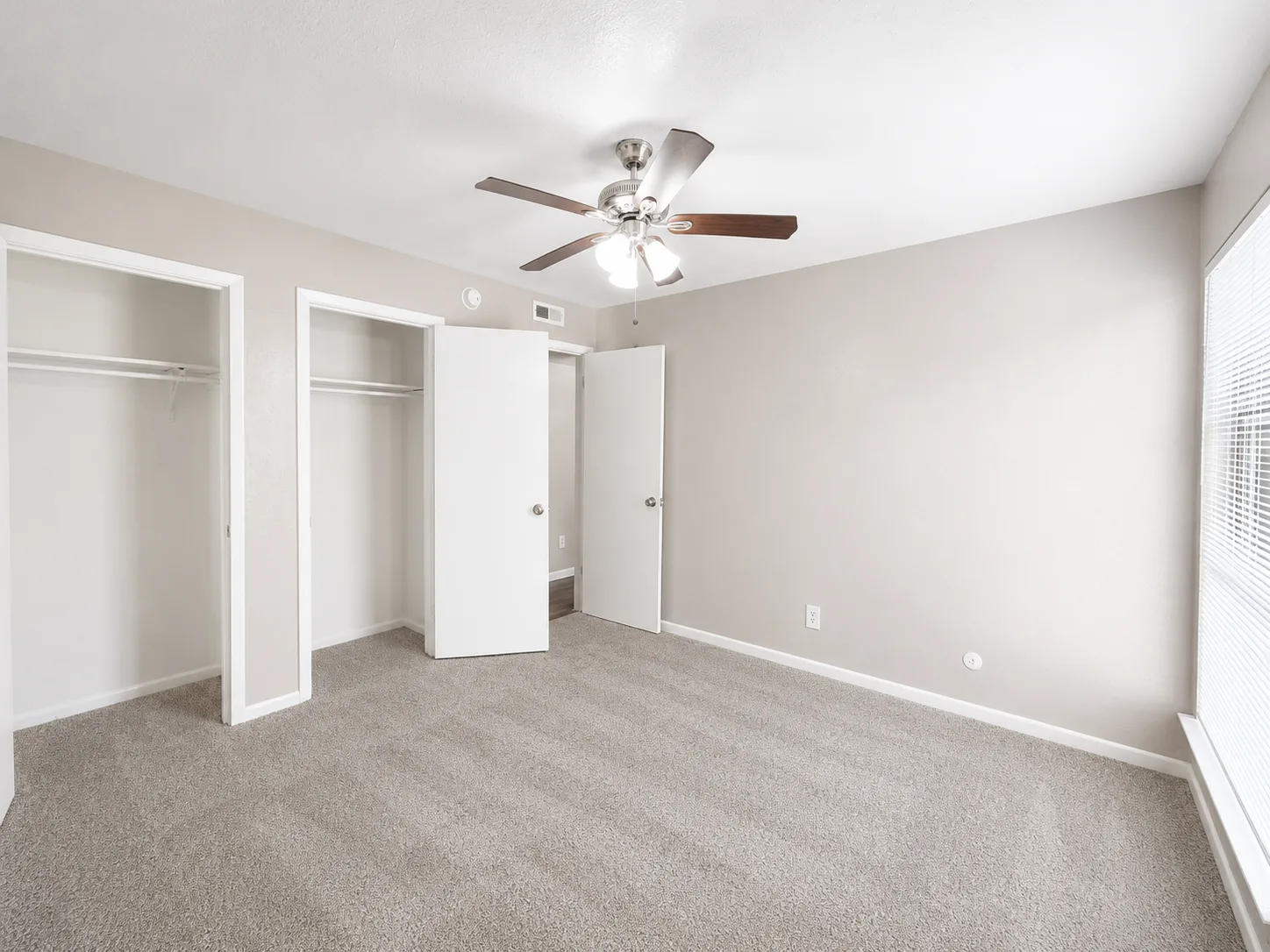 Empty carpeted C1 bedroom with a ceiling fan and two closets, both with hanging rods