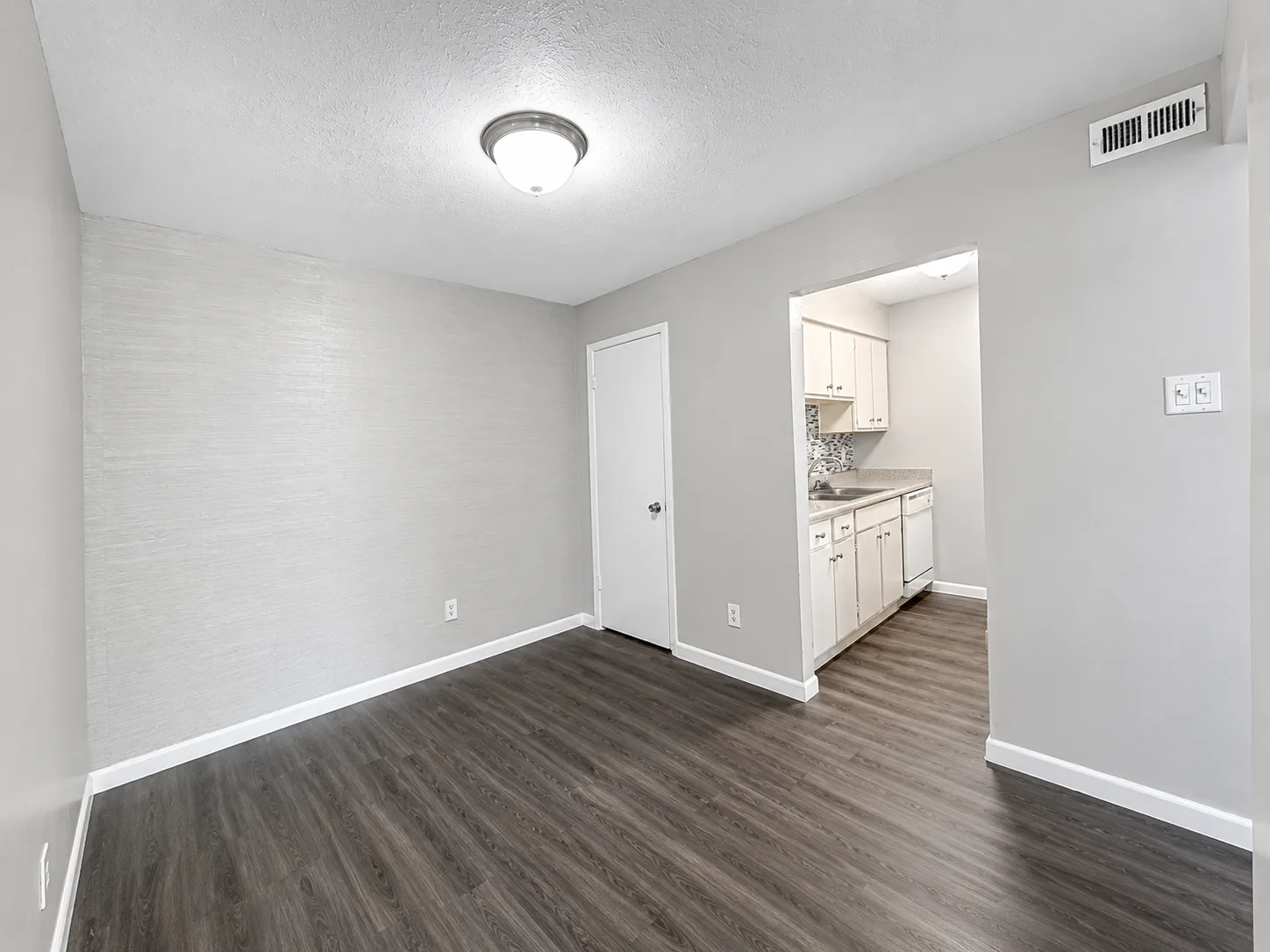 Empty C1 dining area with a textured accent wall, wood-look flooring, and a pass-through to the kitchen with its mosaic tile backsplash