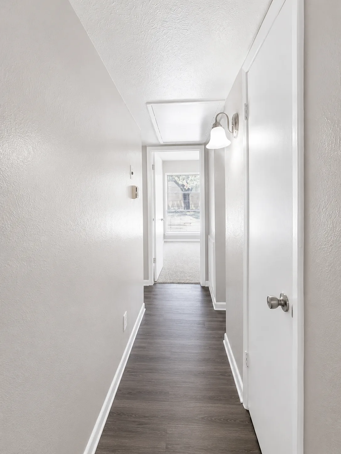 C1 hallway with wood-look flooring and a wall sconce, opening to a carpeted bedroom at the end