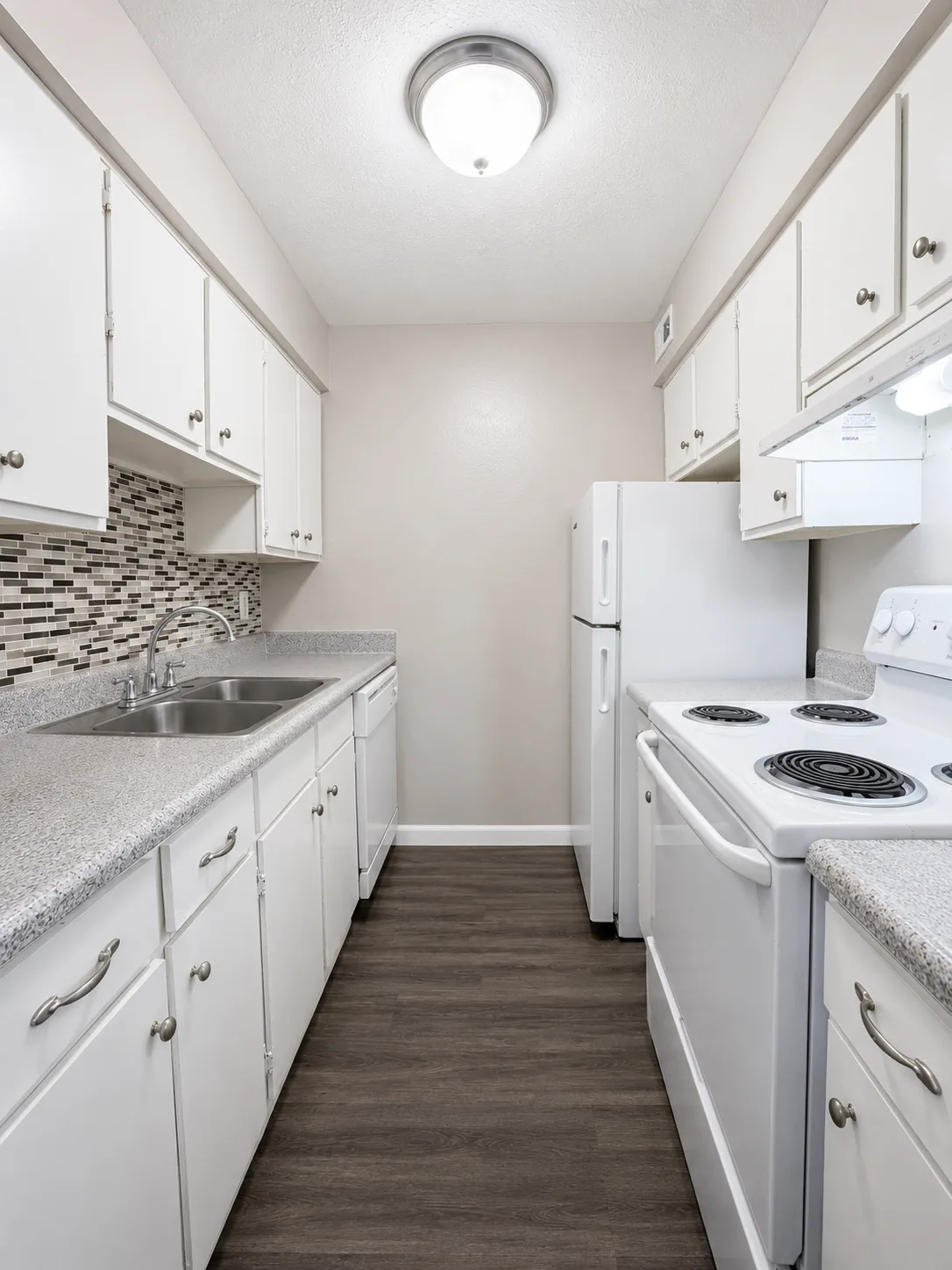 C1 galley kitchen with white cabinets and appliances, a mosaic tile backsplash, speckled counters and a double stainless-steel sink