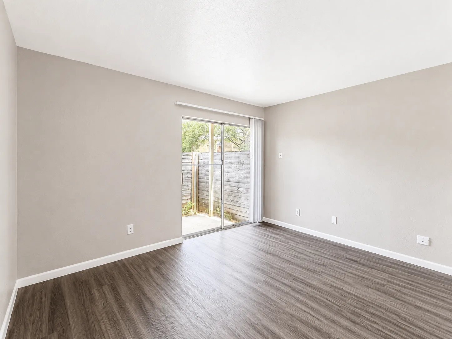 Empty C1 living room with a sliding glass door opening to a wood-fenced private patio