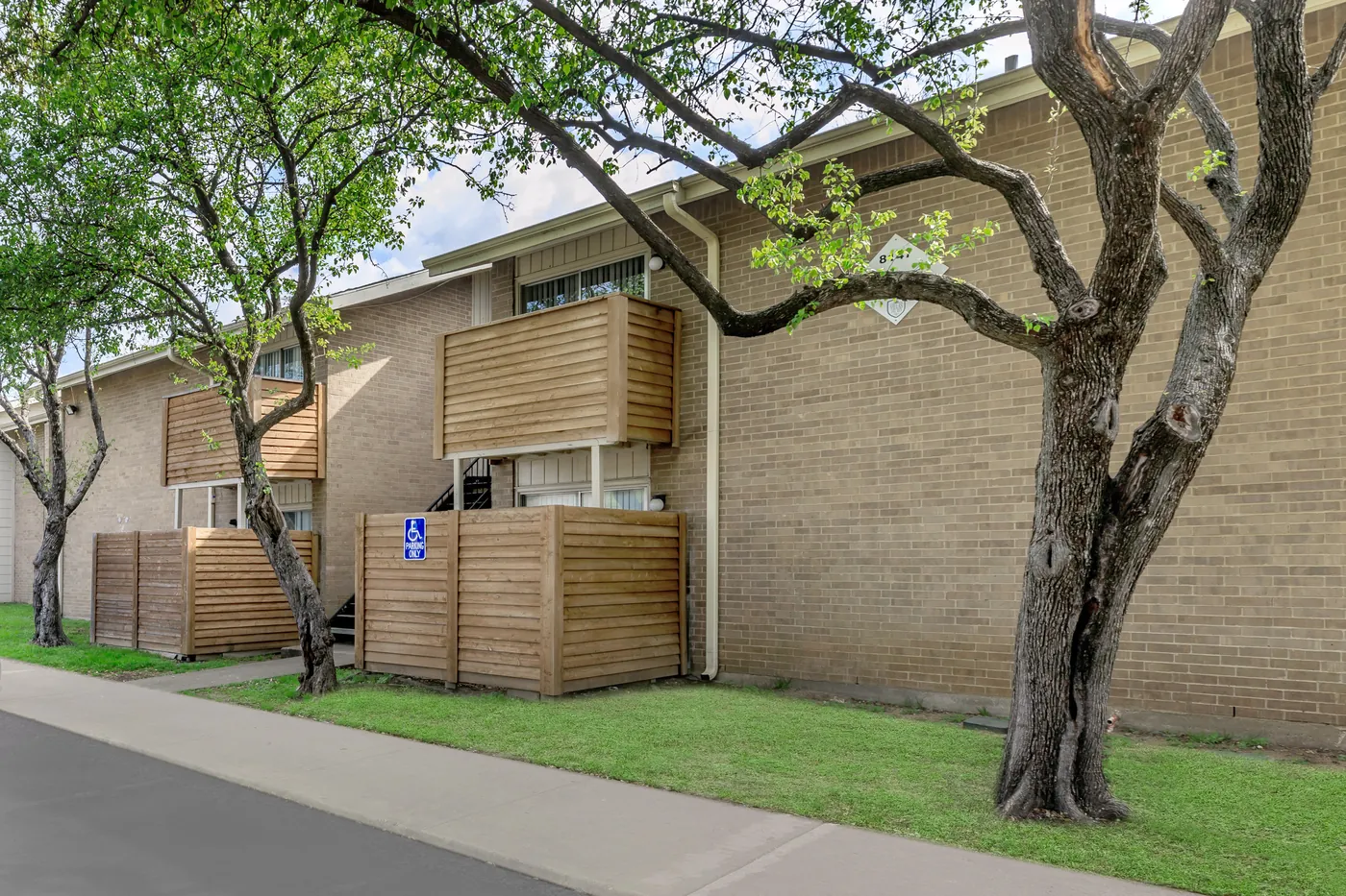 Tan brick building with wood-screened patios beneath a mature shade tree