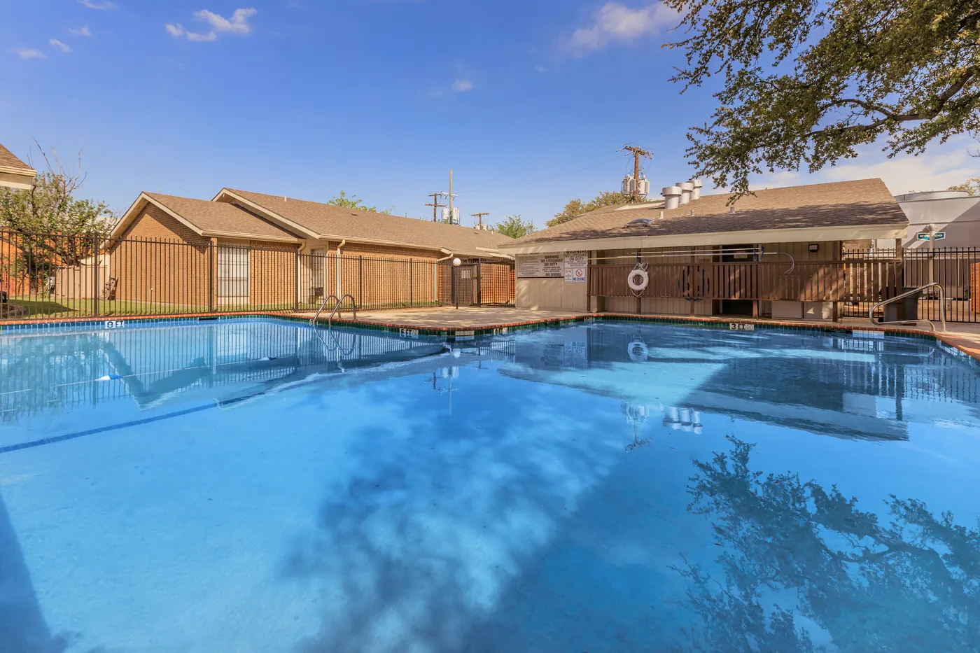 Swimming pool with buildings and mature trees beyond the safety fence